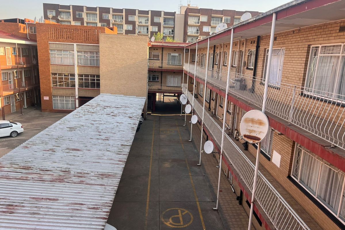 An elevated view of the apartment complex courtyard featuring a covered parking area, multi-level walkways with metal railings, and multiple satellite dish installations.