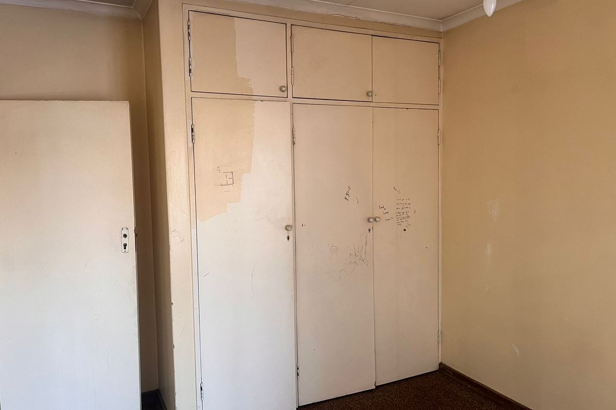 A bedroom featuring built-in storage cupboards with visible wear and surface damage, requiring cosmetic refurbishment.