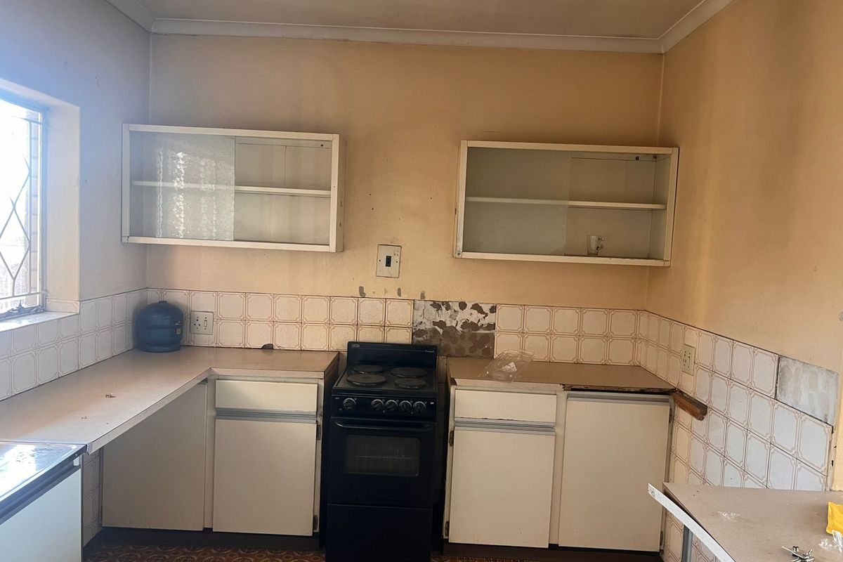 A dated kitchen featuring original cabinetry, a freestanding stove, and tiled splashbacks, requiring significant renovation and modernization to improve functionality and aesthetic appeal.