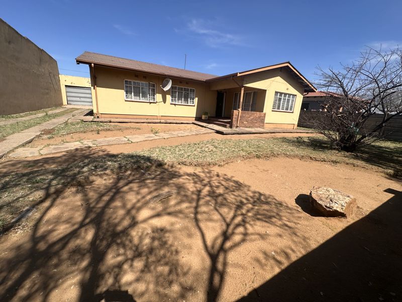 Front view of a single-story house featuring a metal roof, brick facade, and a large, unlandscaped front yard area.