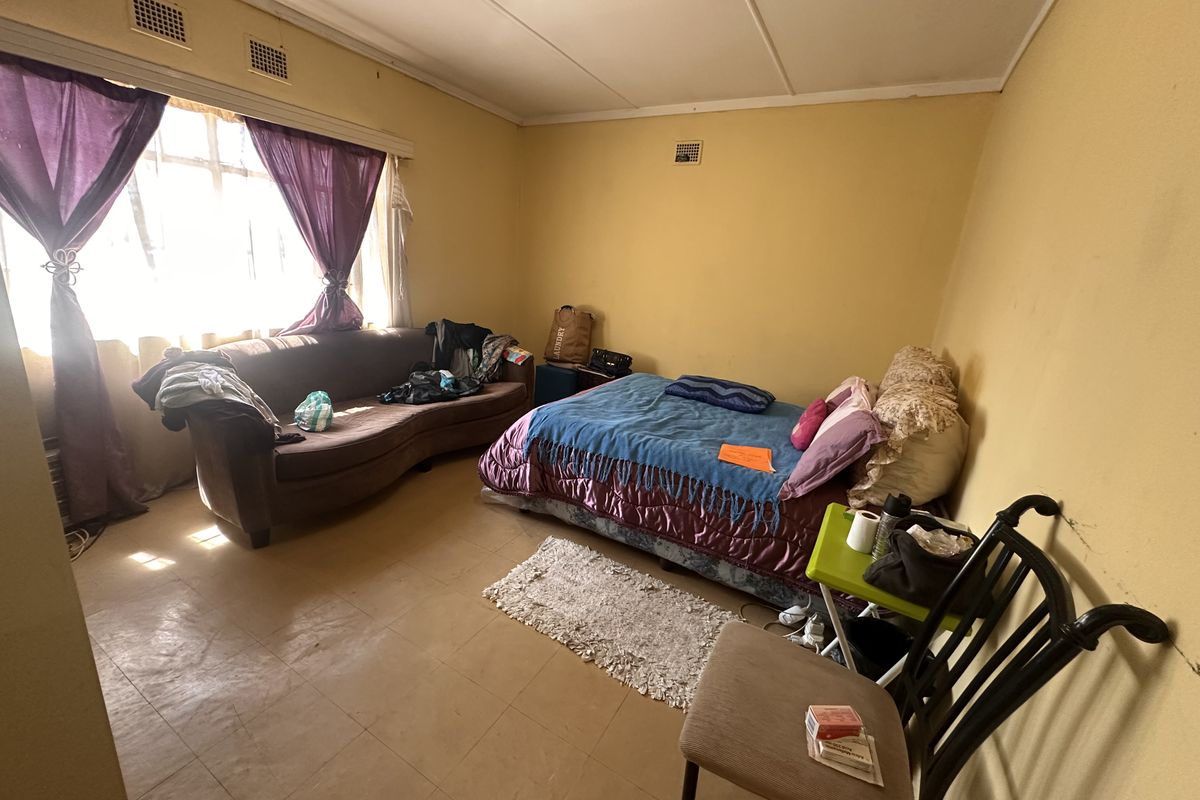A bedroom featuring large windows and ceiling ventilation, currently requiring cosmetic updates to the flooring and wall finishes.