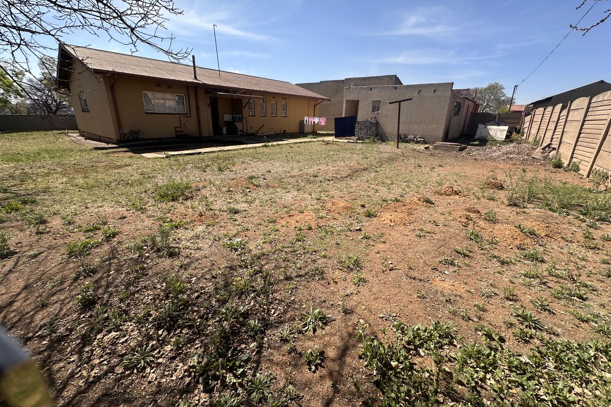 Rear view of the property showing a large, unlandscaped backyard, main house structure, and a detached outbuilding with perimeter walling.