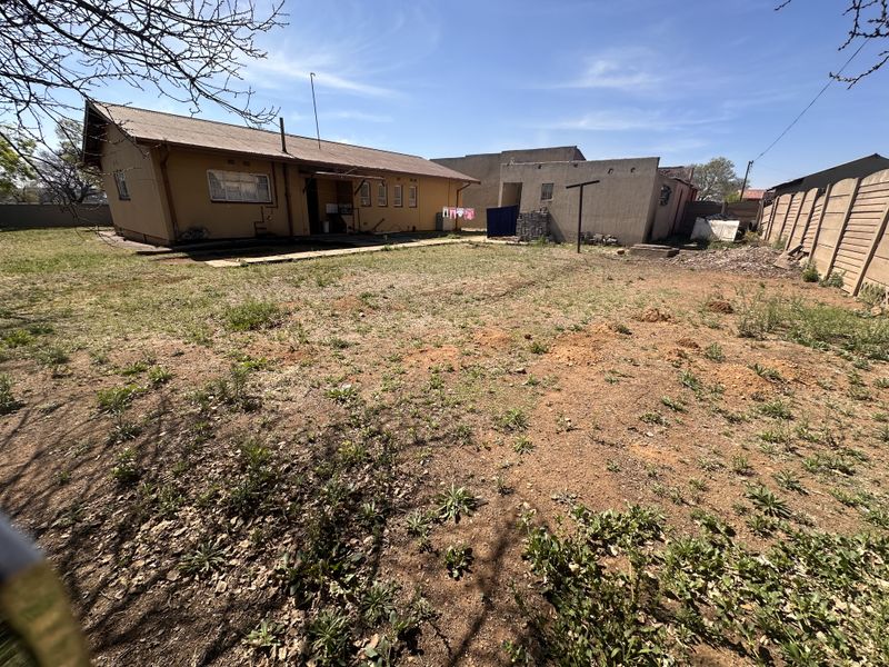 Rear view of the property showing a large, unlandscaped backyard, main house structure, and a detached outbuilding with perimeter walling.
