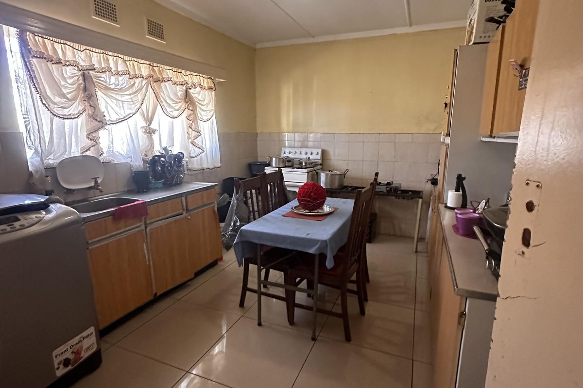 A functional kitchen featuring tiled flooring, built-in cabinetry, and a tiled splashback, offering a practical layout with potential for modern cosmetic updates.