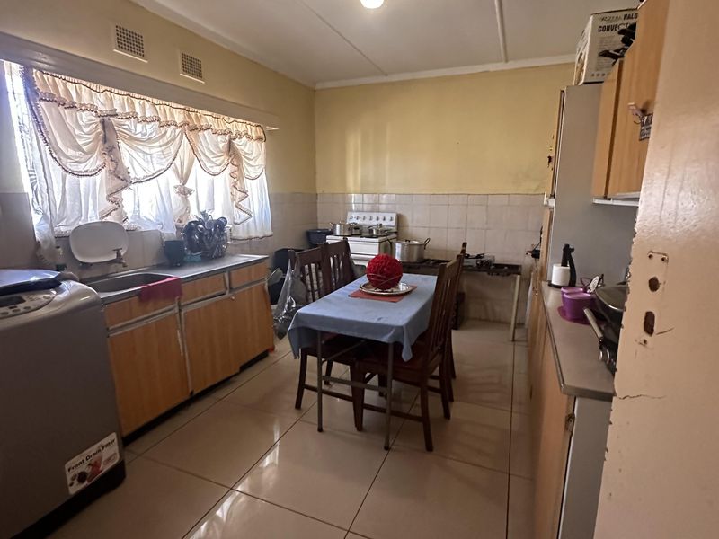 A functional kitchen featuring tiled flooring, built-in cabinetry, and a tiled splashback, offering a practical layout with potential for modern cosmetic updates.