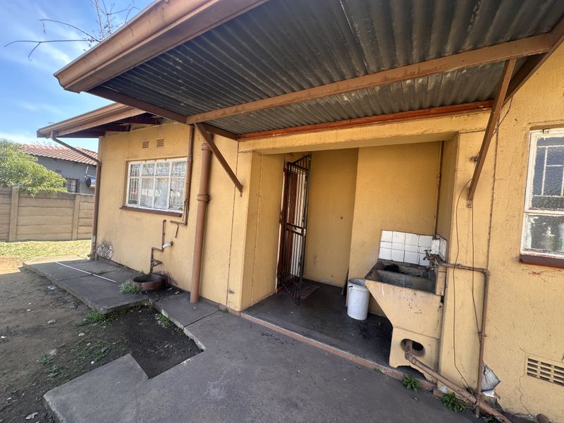 Rear exterior view showing a covered utility area with a concrete wash trough, steel window frames, and signs of significant weathering to the building facade.