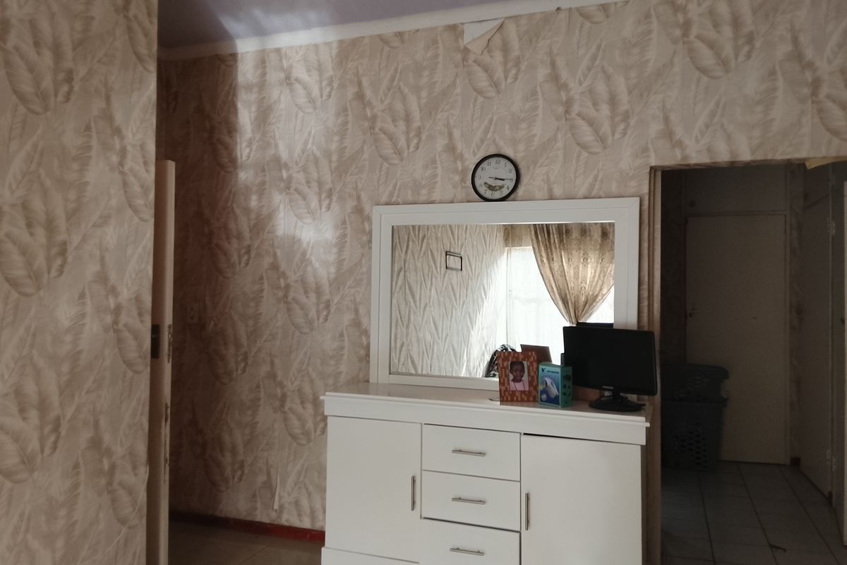 A bedroom featuring patterned wallpaper and tiled flooring, showing signs of wear including peeling wallpaper near the ceiling.