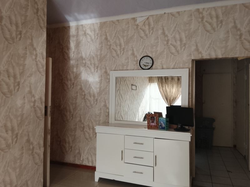 A bedroom featuring patterned wallpaper and tiled flooring, showing signs of wear including peeling wallpaper near the ceiling.