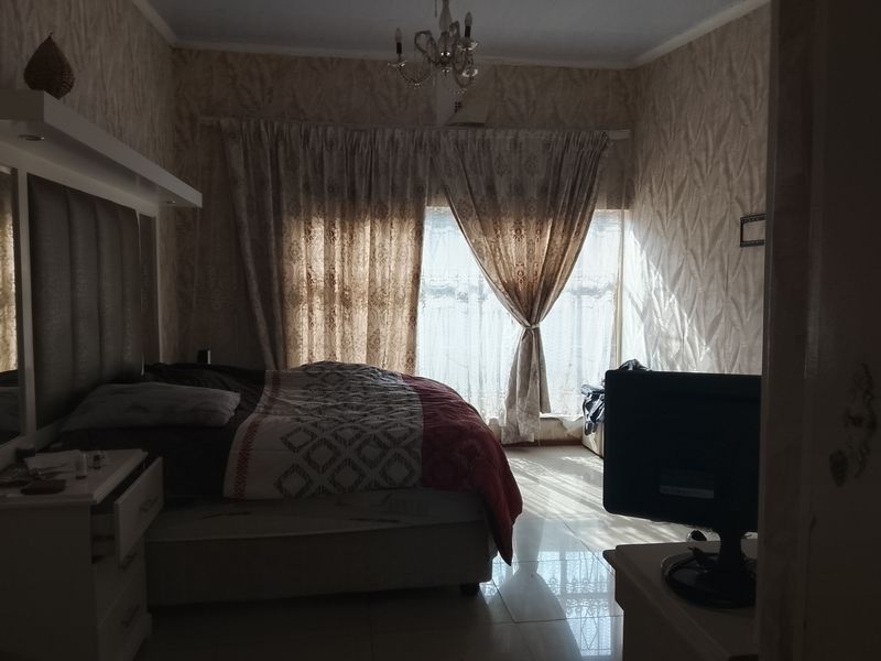 A bedroom featuring tiled flooring, a built-in headboard, and a decorative ceiling chandelier, with natural light entering through the window.