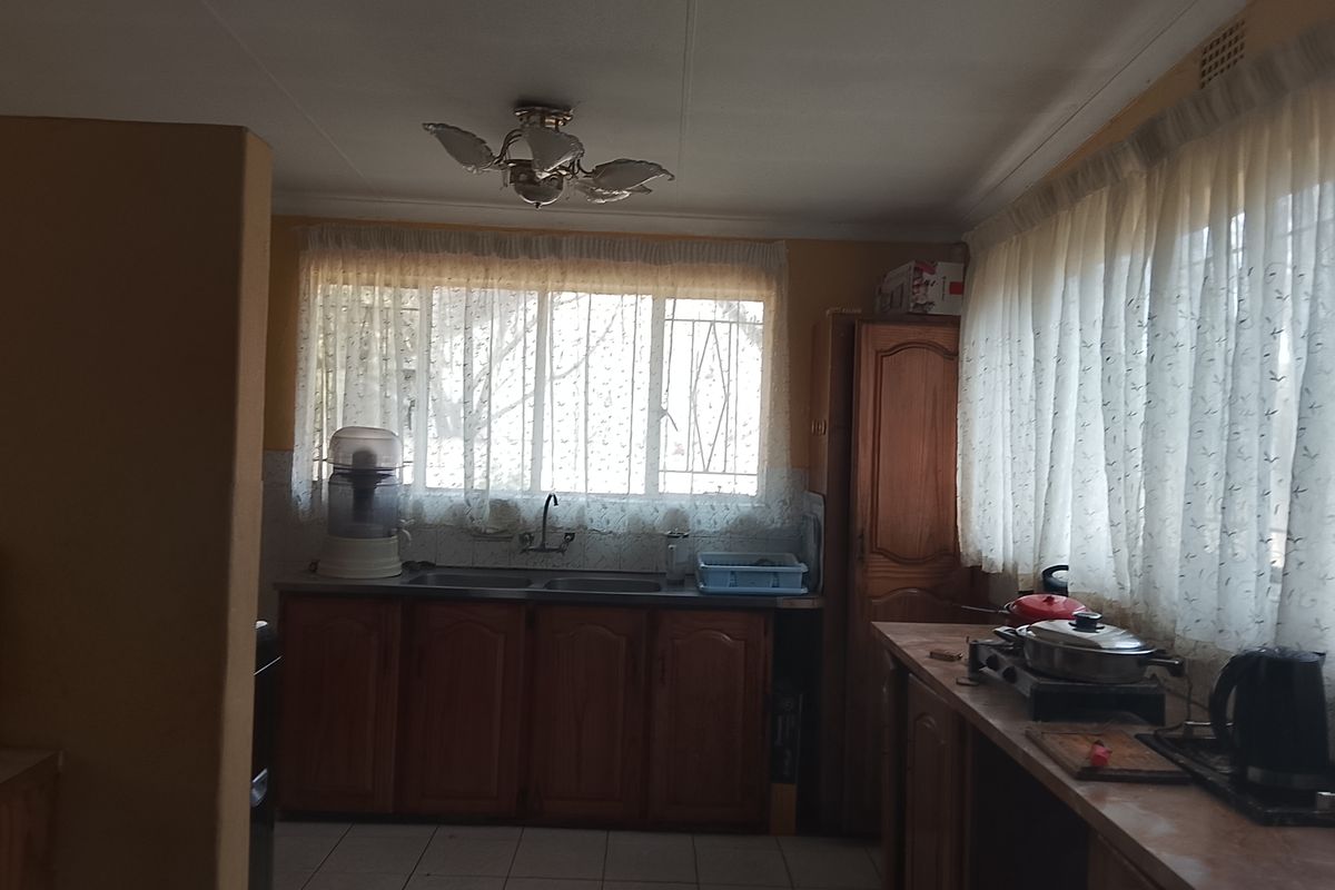 A dated kitchen featuring wooden cabinetry, tiled flooring, and double sink, with security bars on the windows.