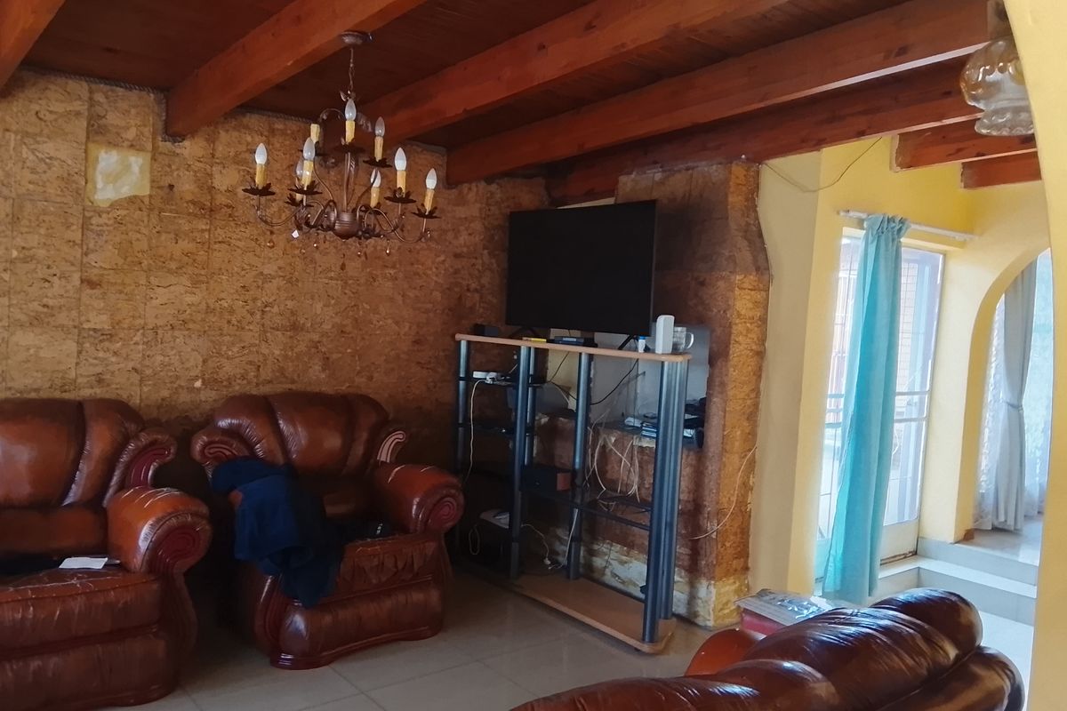 Living room featuring exposed timber ceiling beams, cork wall cladding, and tiled flooring, with an archway leading to an adjacent space.