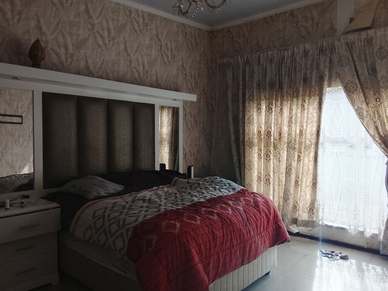 A bedroom featuring a built-in headboard, tiled flooring, and natural light through large window curtains.