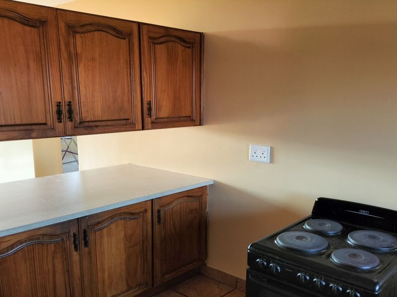 A functional kitchen area featuring traditional wooden cabinetry, laminate countertops, and a freestanding electric stove.