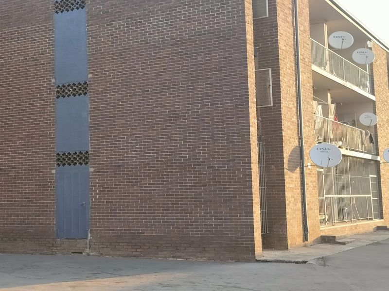 Exterior view of a multi-story apartment building featuring a brick facade, private balconies with security gates, and multiple satellite dish installations.