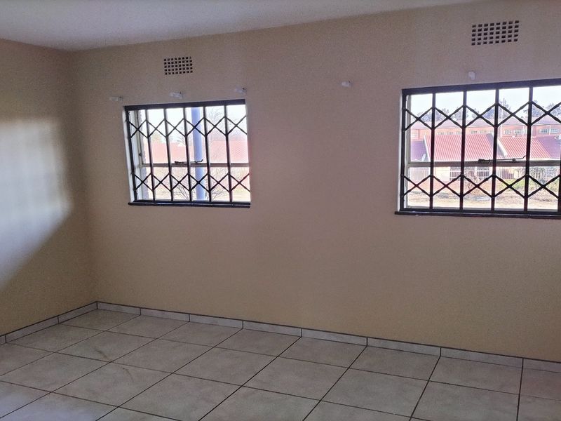 A clean, empty bedroom featuring neutral wall paint, tiled flooring, and windows fitted with security bars for added safety.
