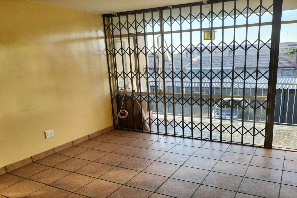 An empty living room featuring ceramic floor tiles and a large sliding glass door secured with a metal security gate.