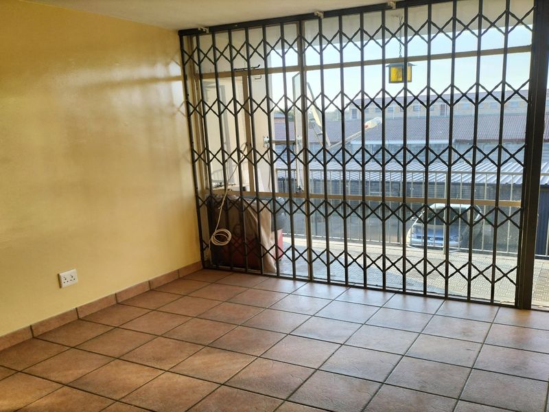 An empty living room featuring ceramic floor tiles and a large sliding glass door secured with a metal security gate.