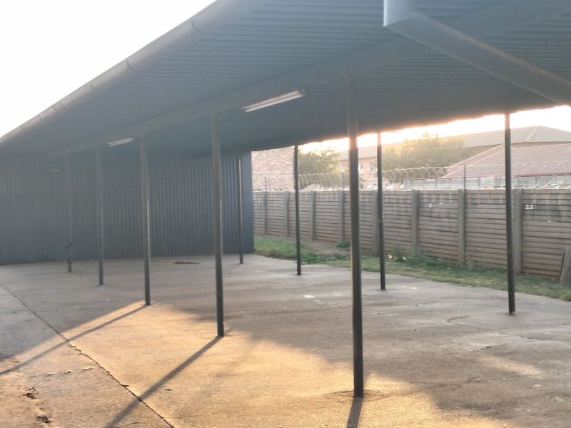 A covered outdoor carport area with a metal roof structure and concrete flooring, providing sheltered parking space.