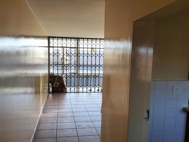 A view through a hallway leading to a balcony with a security gate, adjacent to a kitchen area with built-in cabinetry and tiled surfaces.