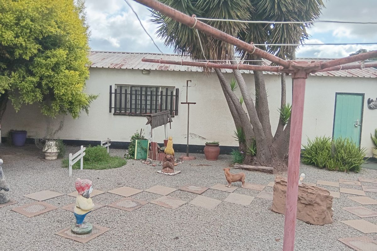 Rear exterior view of the property featuring a gravel garden, paved pathways, and a rotary clothesline against a white rendered wall.