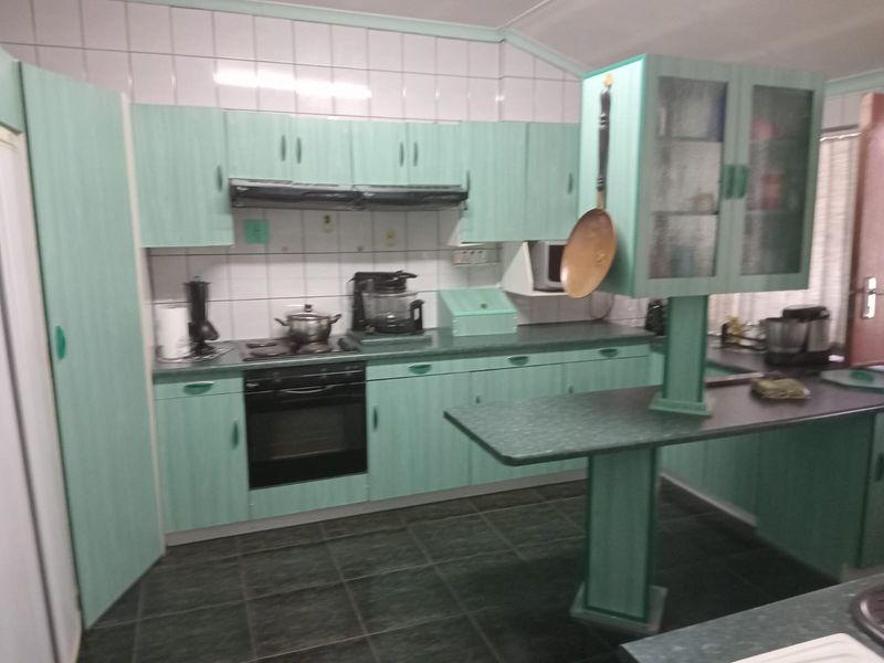 A dated kitchen featuring mint green cabinetry, dark laminate countertops, tiled backsplash, and integrated oven with extractor fan.