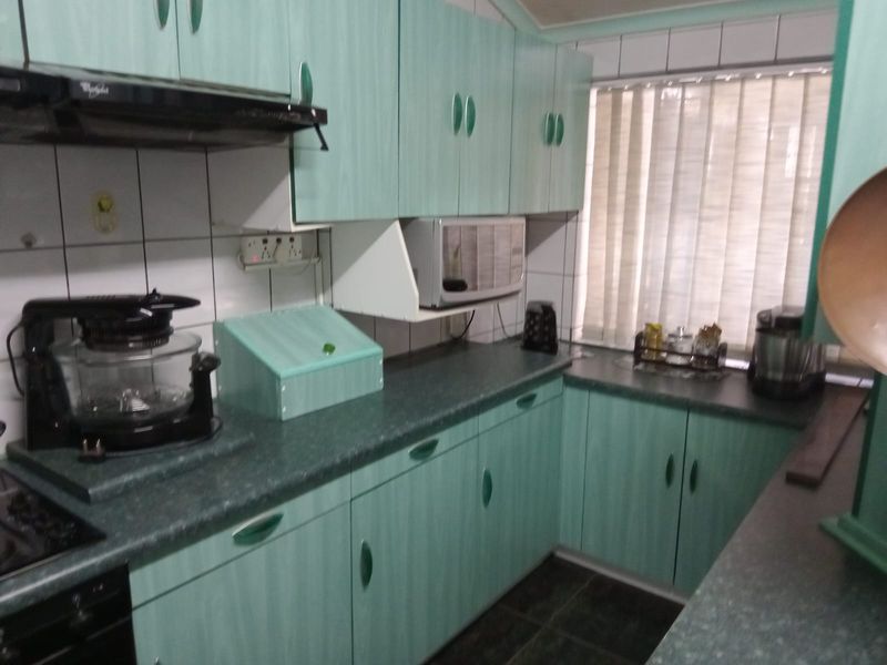 A functional kitchen featuring dated green laminate cabinetry, dark countertops, tiled backsplash, and integrated appliances, offering potential for a modern renovation.
