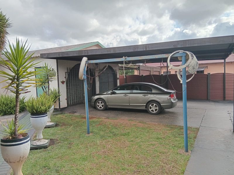 Front exterior view featuring a paved driveway, a metal carport structure, and secure gated access to the main dwelling.