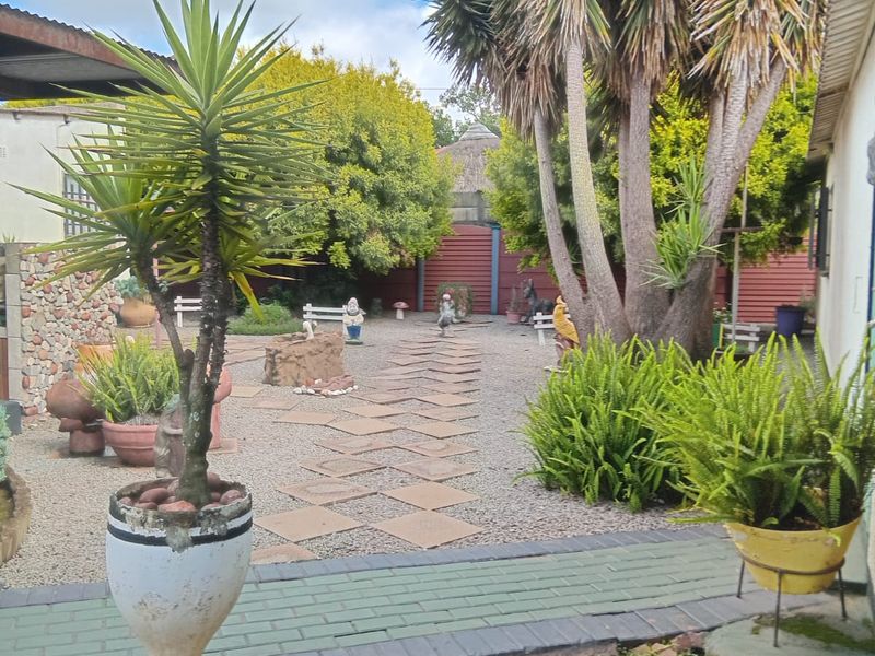 A landscaped garden area featuring a paved walkway, gravel ground cover, mature trees, and a covered patio edge.