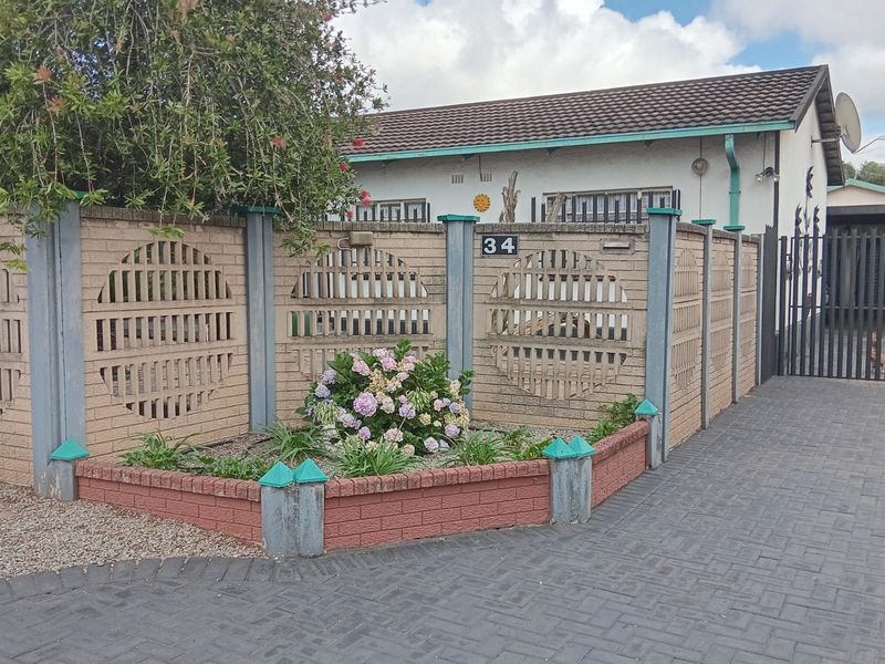 Front view of the property featuring a paved driveway, decorative brick boundary wall with security gate, and a raised garden bed.
