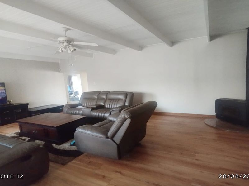 Spacious living room featuring exposed beam ceilings, laminate flooring, and a built-in wood-burning stove.