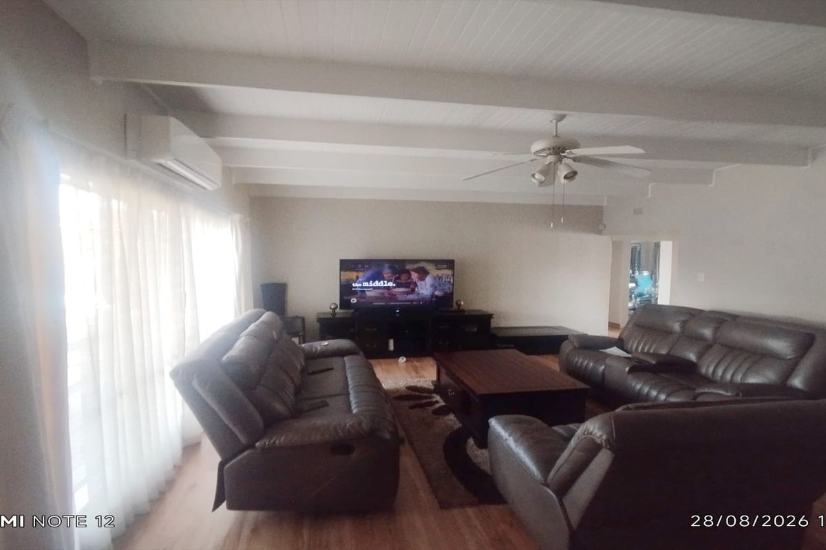 Spacious living room featuring exposed beam ceilings, a ceiling fan, and a wall-mounted air conditioning unit with laminate flooring throughout.