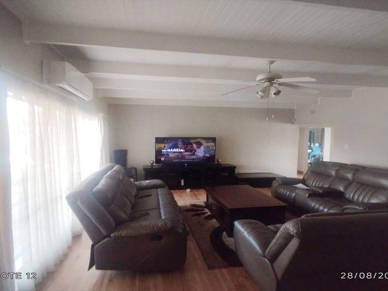Spacious living room featuring exposed beam ceilings, a ceiling fan, and a wall-mounted air conditioning unit with laminate flooring throughout.
