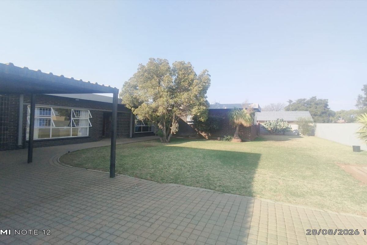 Spacious rear garden featuring a paved patio area with a covered pergola, established lawn, and brick exterior walls.