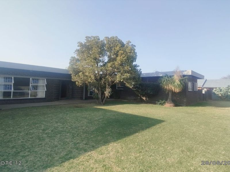 A view of the rear exterior of the house featuring a brick facade, paved walkway, and a well-maintained lawn.