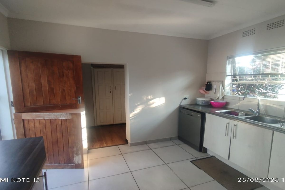 A functional kitchen area featuring tiled flooring, built-in cabinetry, a stainless steel sink, and a traditional stable door leading to an adjacent room.
