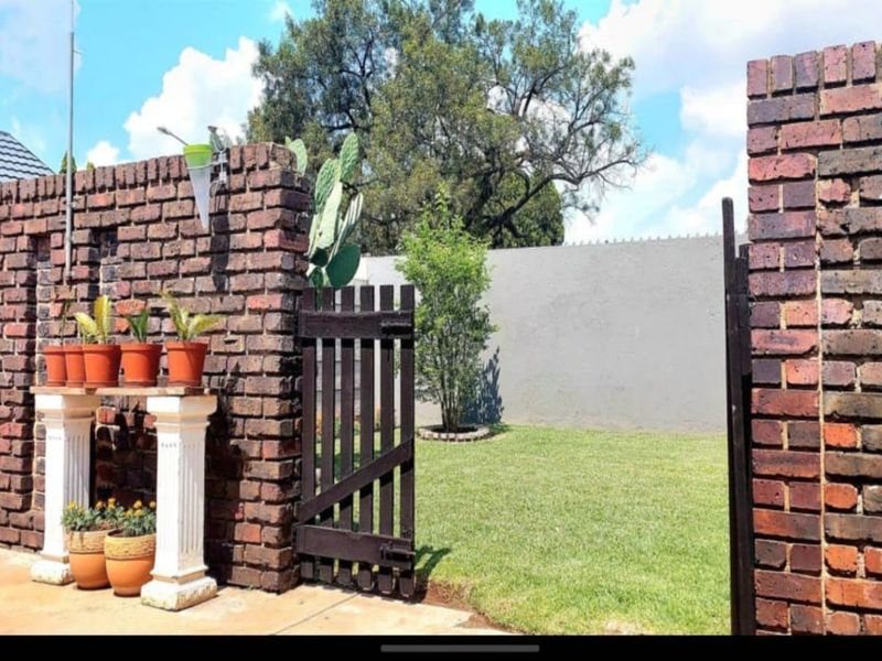 A private garden area featuring a rustic brick boundary wall, a timber gate, and a well-maintained lawn.