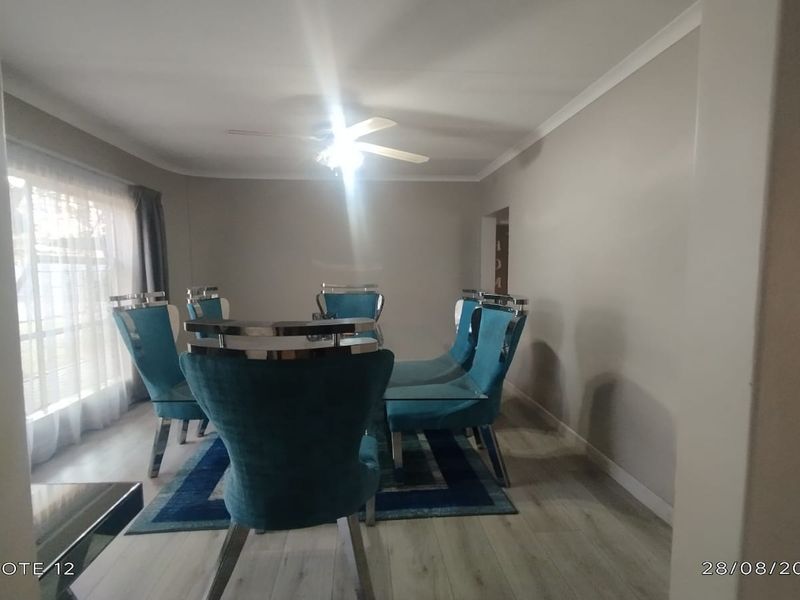 A well-maintained dining room featuring light-toned laminate flooring, a central ceiling fan, and neutral wall finishes.