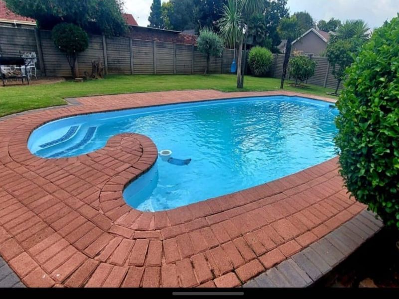 A well-maintained swimming pool area featuring a curved design, brick paved surround, and a spacious lawn enclosed by a precast concrete boundary wall.