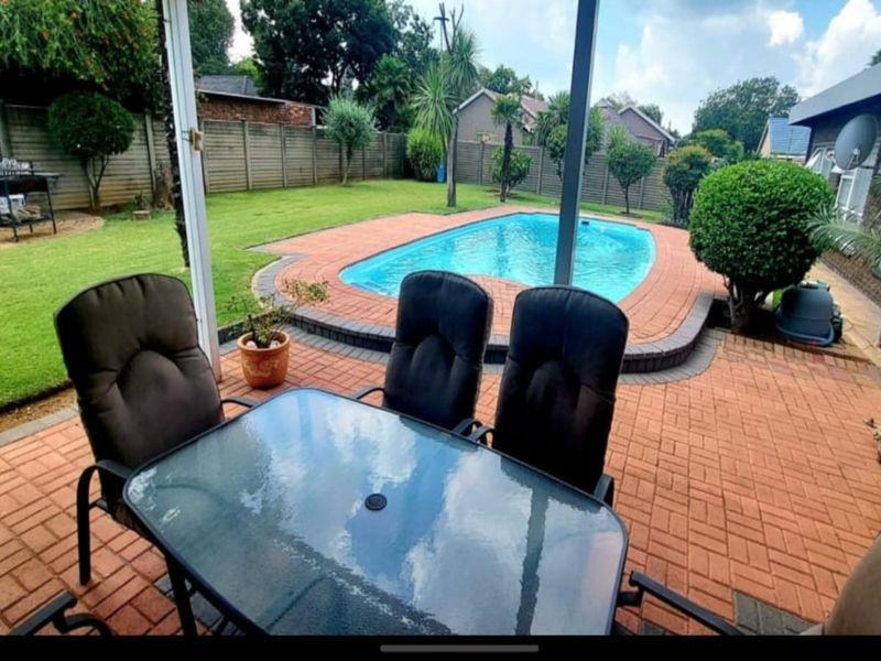 Outdoor entertainment area featuring a brick-paved patio, covered seating space, and a swimming pool set within a private, walled garden.