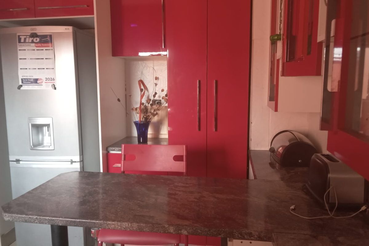 A kitchen area featuring red high-gloss cabinetry, a stone-topped breakfast bar, and integrated storage space.
