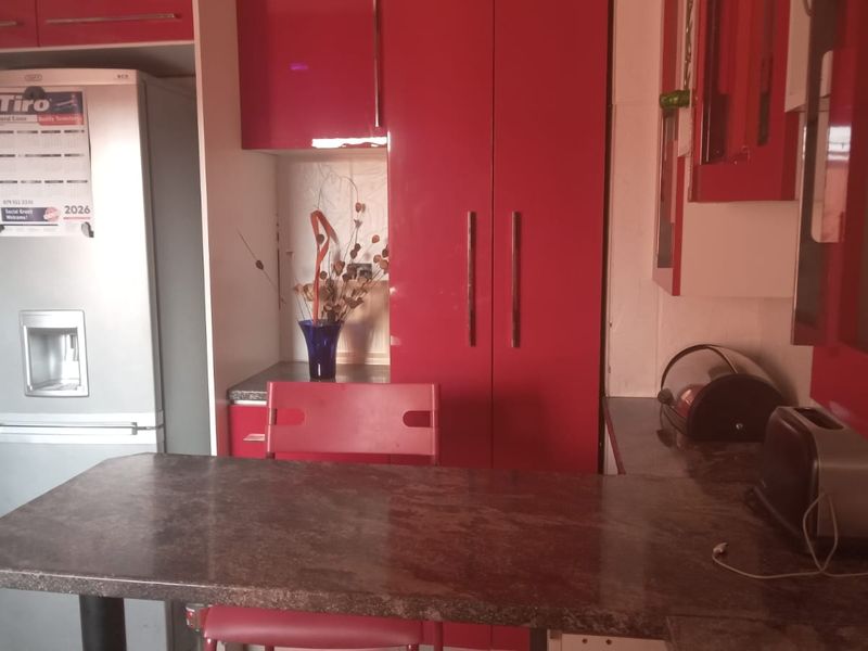 A kitchen area featuring red high-gloss cabinetry, a stone-topped breakfast bar, and integrated storage space.