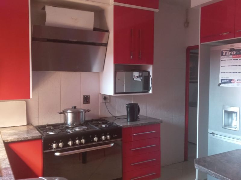 A functional kitchen featuring vibrant red cabinetry, a gas stove with extractor fan, built-in microwave, and stone-look countertops.