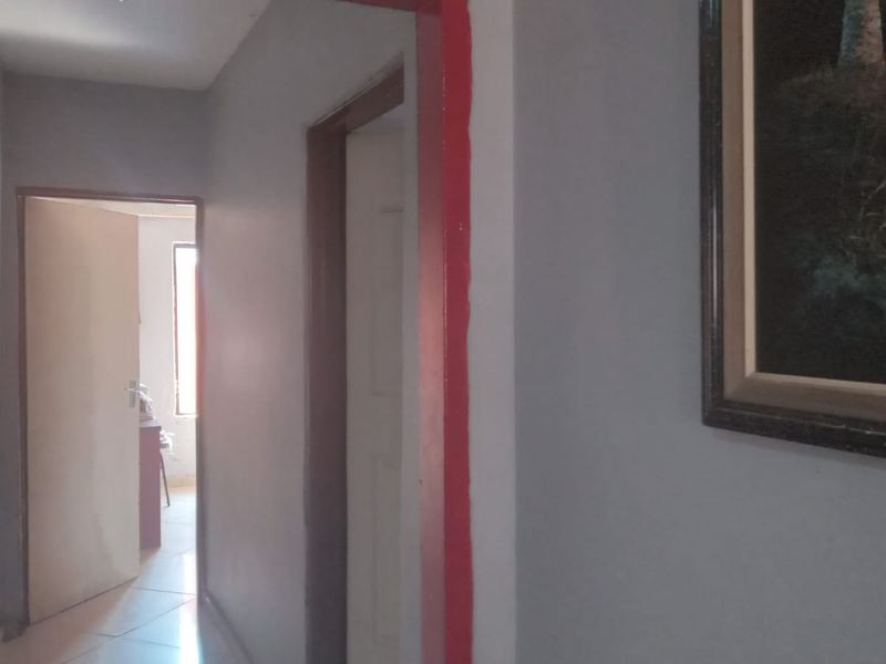A simple interior hallway featuring tiled flooring and painted door frames, providing access to adjacent rooms within the property.