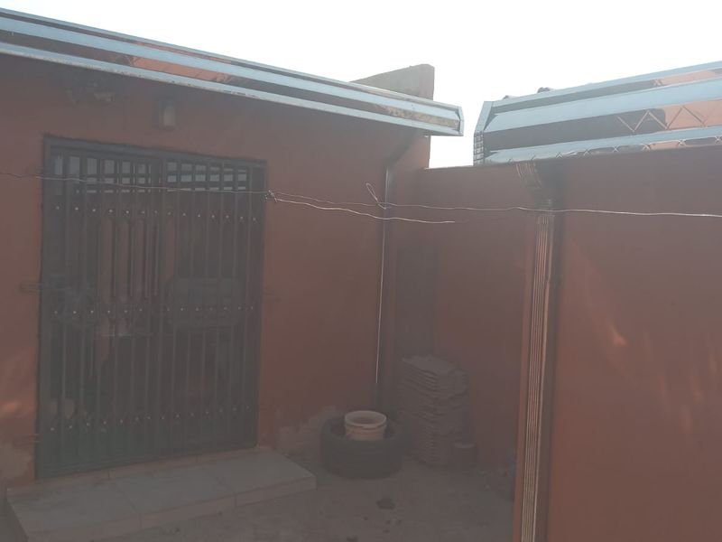 Rear exterior view of the property featuring a security gate, guttering system, and painted masonry walls showing signs of wear.