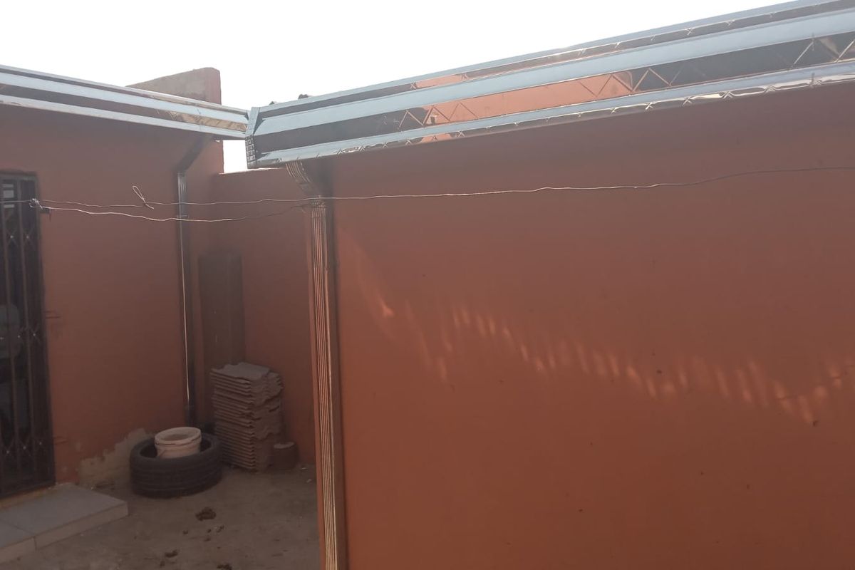 Rear exterior view of the property showing installed metal guttering, downpipes, and a security gate on the entrance door.