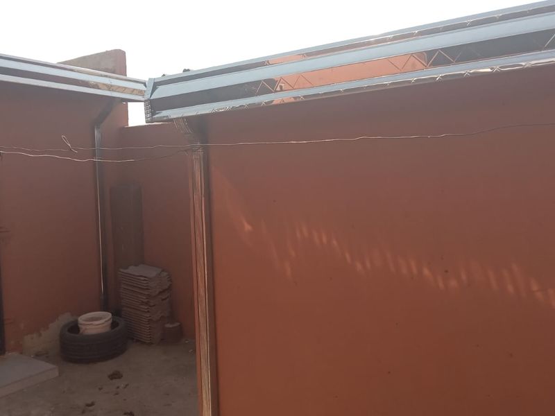 Rear exterior view of the property showing installed metal guttering, downpipes, and a security gate on the entrance door.
