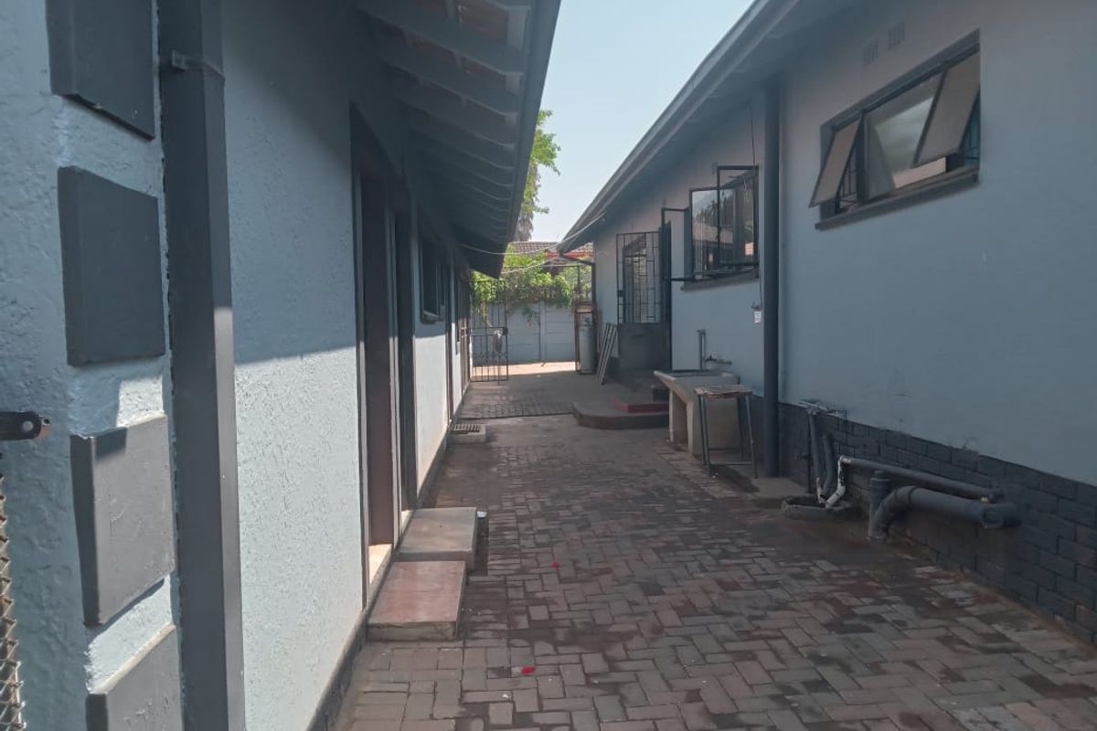 A paved side passage between two building sections featuring an external wash basin, security bars on windows, and exposed exterior plumbing.