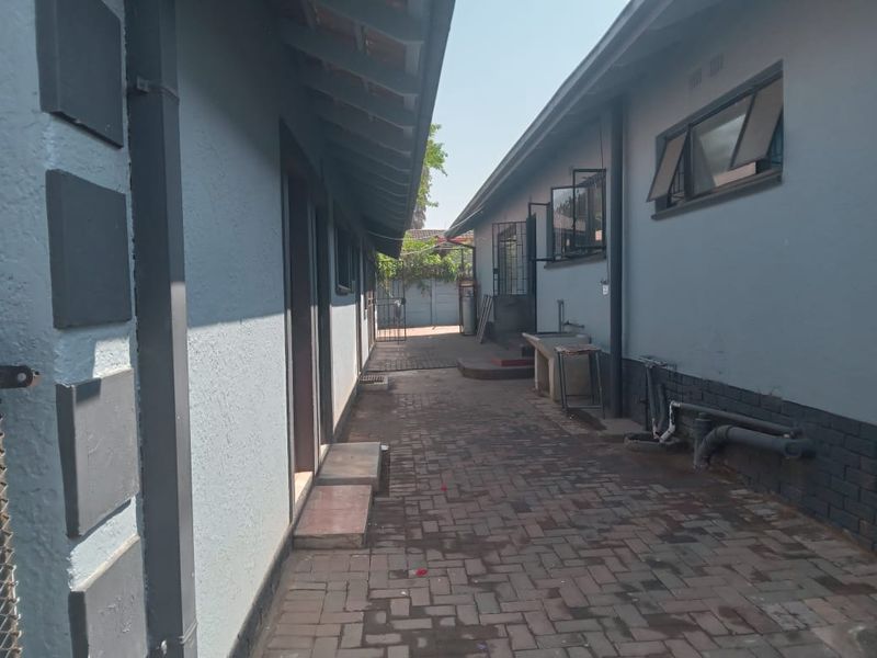 A paved side passage between two building sections featuring an external wash basin, security bars on windows, and exposed exterior plumbing.