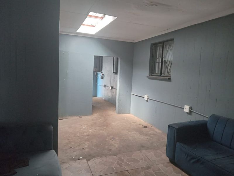An interior living space featuring a skylight, exposed electrical conduit, and tiled flooring, currently requiring significant cosmetic updates and finishing work.