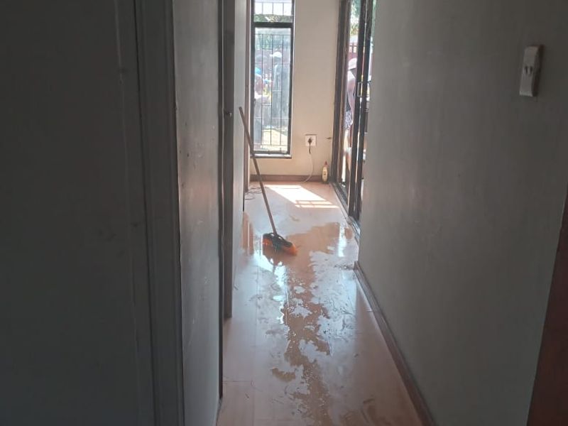 A narrow hallway featuring laminate flooring and a sliding glass door, currently showing signs of water accumulation on the floor surface.